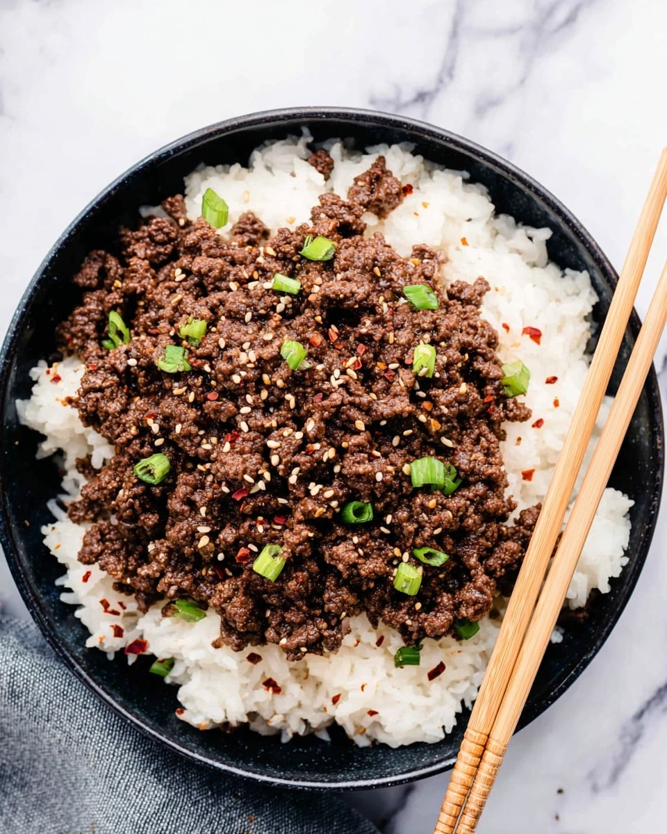 A black bowl filled with two main layers: the bottom layer is white rice with a soft, fluffy texture, covering the whole base of the bowl. On top, there is a thick layer of cooked ground beef, dark brown and crumbly, spread evenly. Small pieces of chopped green onions are sprinkled on the beef, adding pops of bright green color. White sesame seeds and red chili flakes are scattered over the top, giving extra texture and color contrast. Two light brown wooden chopsticks rest on the right side of the bowl, slightly inserted into the beef layer. The bowl sits on a white marbled surface. Photo taken with an iphone --ar 4:5 --v 7