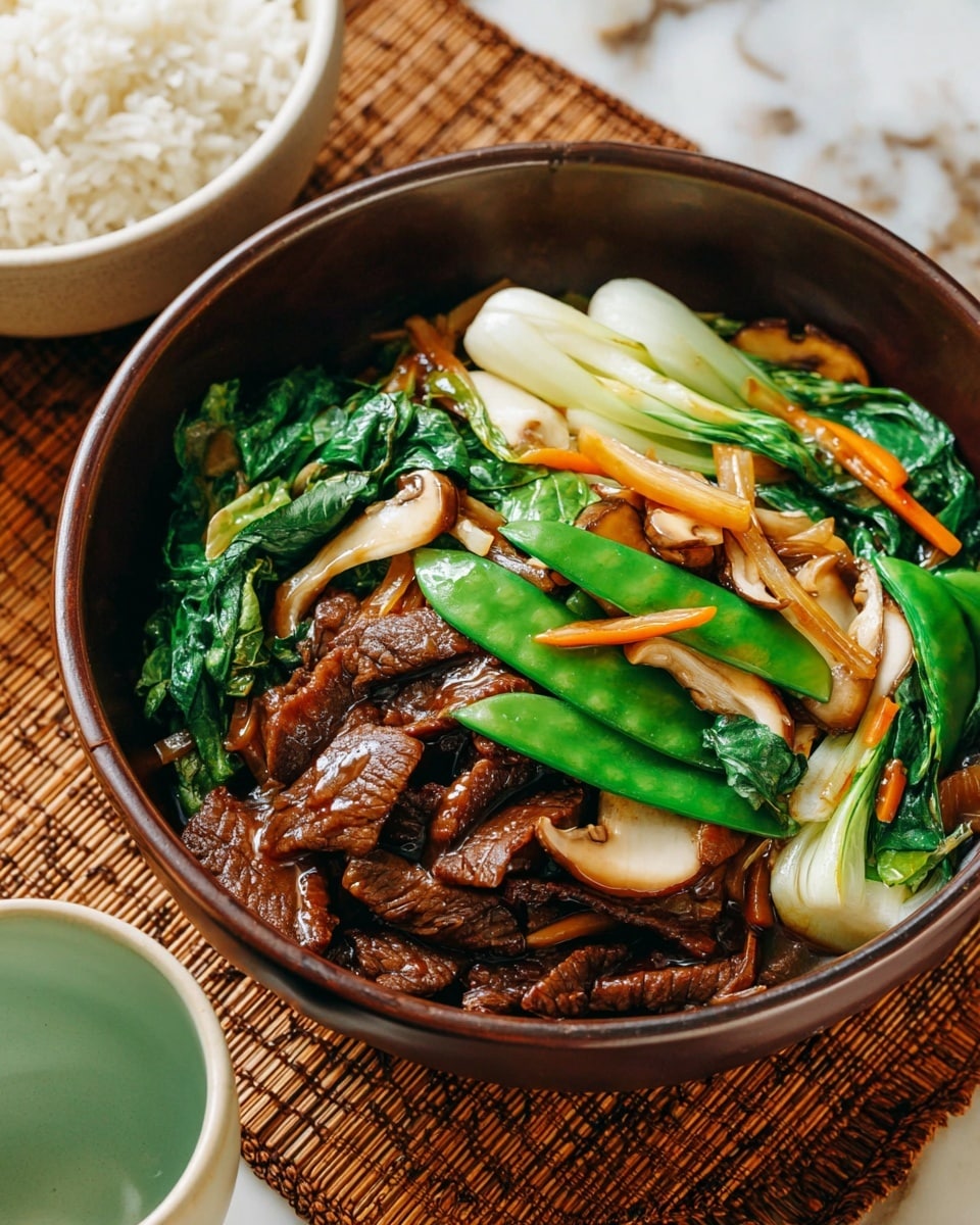 A dark brown bowl filled with a stir-fry dish featuring three main layers: the bottom layer is a glossy brown sauce, the middle layer has brown, thinly sliced cooked beef pieces, and the top layer includes vibrant green snap peas, bright green leafy vegetables, creamy white and light brown bok choy stems, and thin orange mushrooms. The bowl sits on a brown woven mat, with a white bowl of plain white rice and a light green cup nearby, all placed on a white marbled surface. photo taken with an iphone --ar 4:5 --v 7