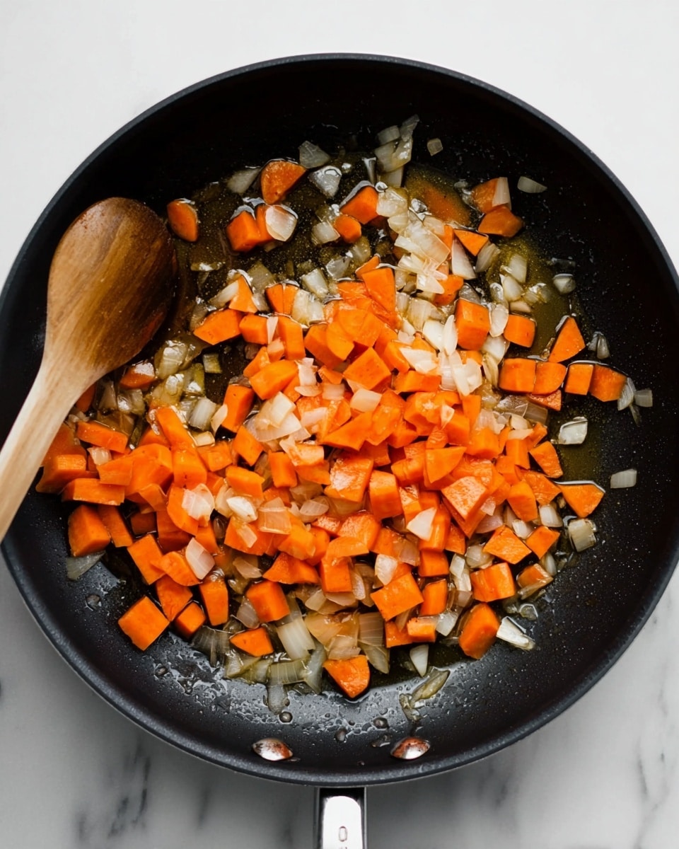 A black frying pan filled with two layers of ingredients: the bottom layer is a glossy layer of oil with some cooked bits, and the top layer is a mix of bright orange chopped carrot pieces and translucent white sautéed onion pieces scattered evenly across the pan. A light brown wooden spoon rests on the edge of the pan at the top left side. The pan is set on a white marbled surface. photo taken with an iphone --ar 4:5 --v 7