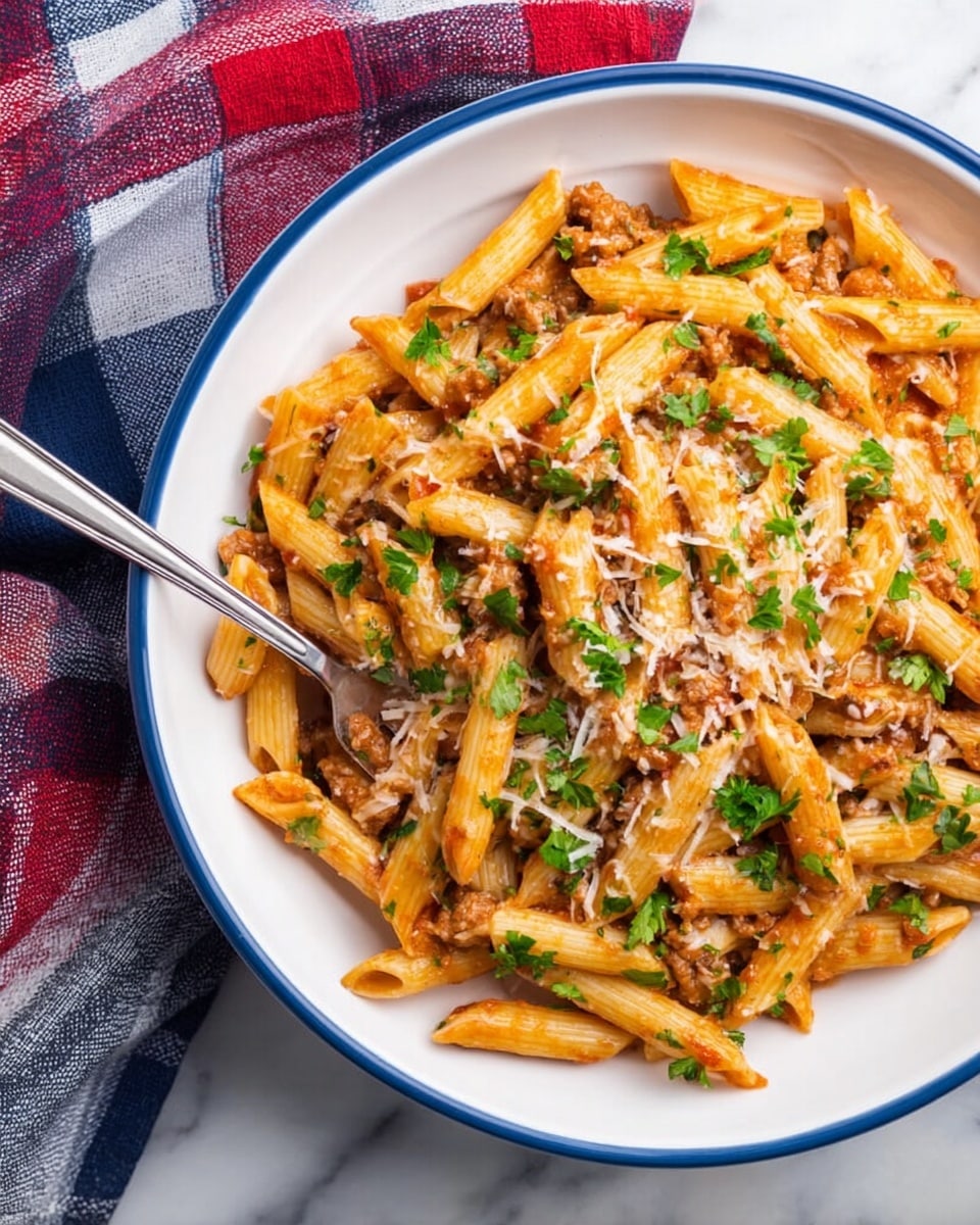 A white bowl with a blue rim is filled with penne pasta coated in a light reddish sauce mixed with small pieces of brown meat. The pasta is sprinkled with finely grated cheese and small bright green parsley leaves, creating a colorful contrast. A silver fork rests inside the bowl, partially buried under the pasta. The bowl is placed on a white marbled surface with a folded red, white, blue, and dark plaid cloth nearby. Photo taken with an iphone --ar 4:5 --v 7