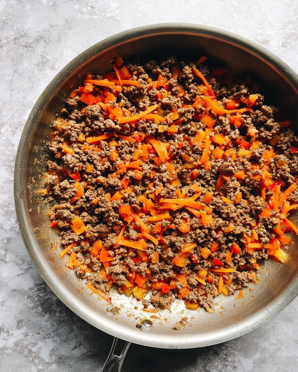 A shiny stainless steel pan filled with cooked ground meat mixed with small orange-red diced bell peppers and thin strips of bright orange carrots, evenly spread across the pan's surface, showing a textured and slightly oily look; the background is a white marbled surface. photo taken with an iphone --ar 4:5 --v 7