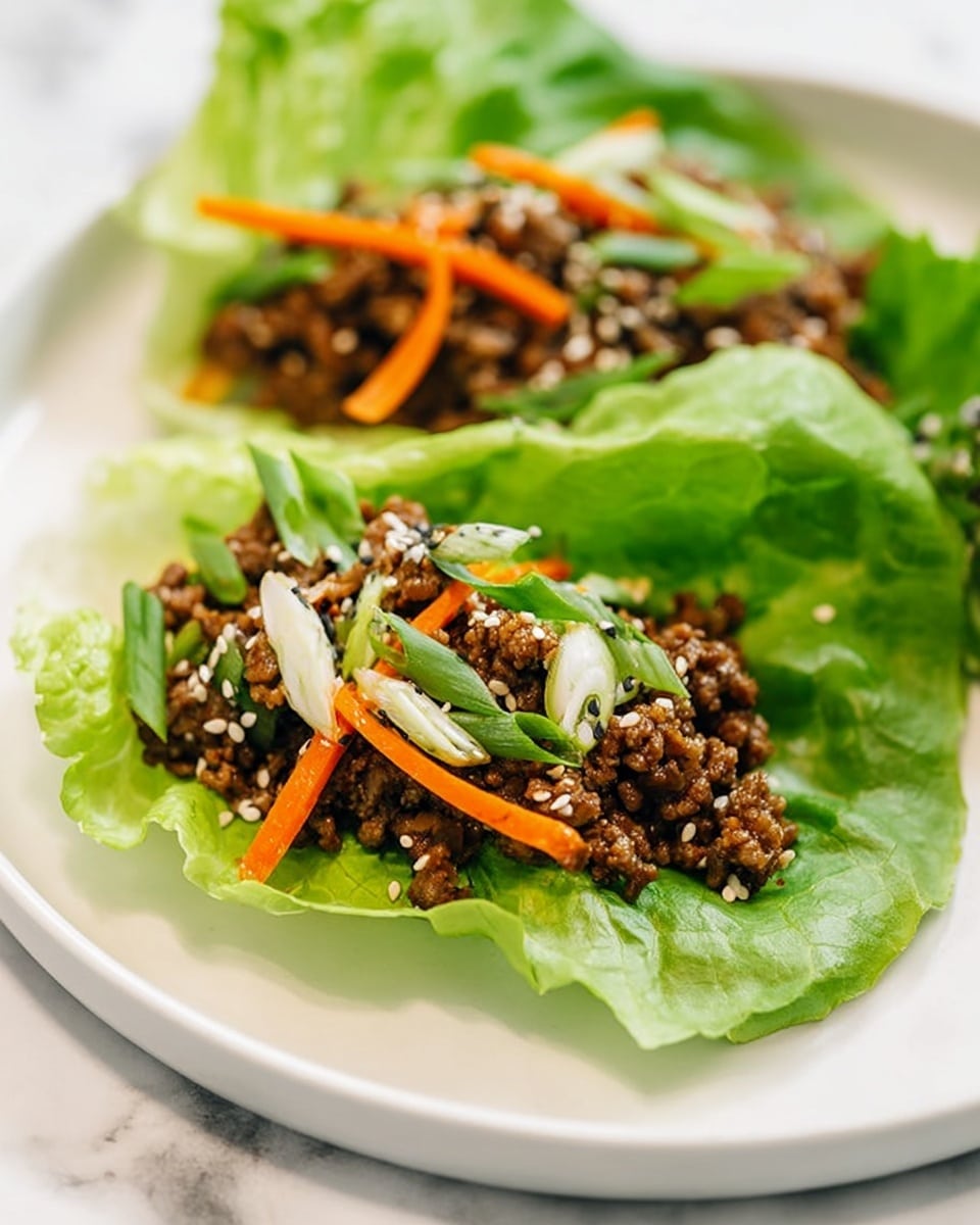 Two lettuce wraps sit on a white plate over a white marbled surface. Each wrap has one bright green lettuce leaf as the base layer, looking fresh and slightly crinkled. On top, there is a mix of small brown cooked meat pieces mixed with thin orange carrot strips and green onion slices. The meat mixture is sprinkled with white and black sesame seeds, adding contrast and texture. The photo taken with an iphone --ar 4:5 --v 7