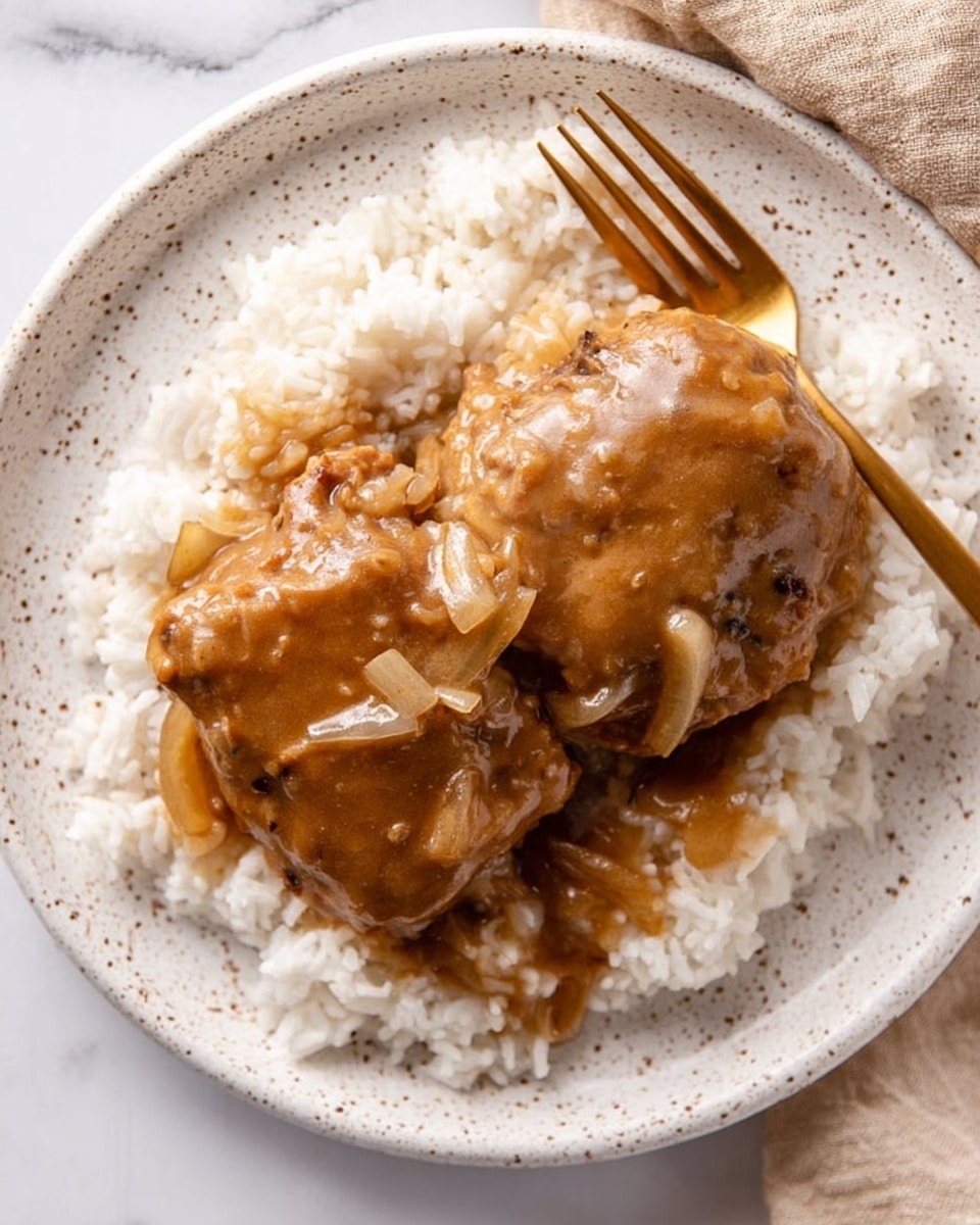 The image shows a white speckled plate on a white marbled surface, holding a bed of white rice as the bottom layer. On top of the rice, there are two large pieces of cooked meat covered in thick brown gravy with visible bits of cooked onions, giving a smooth and slightly textured look to the sauce. Next to the food, a gold fork rests on the plate, adding a touch of color contrast. The photo taken with an iphone --ar 4:5 --v 7