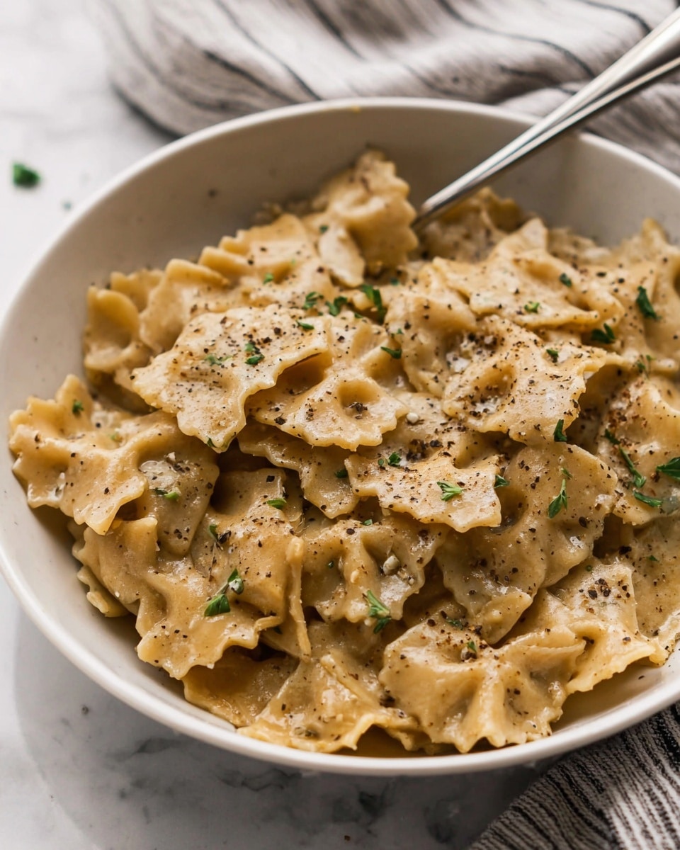 A white bowl filled with short, wide pasta pieces that have wavy edges, all covered in a creamy light brown sauce. The pasta is soft and coated evenly, with small green herb leaves scattered on top and fine black pepper sprinkled over it. A silver fork rests inside the bowl, leaning against the side. The background features a white marbled surface with a soft-focus striped cloth nearby. Photo taken with an iphone --ar 4:5 --v 7