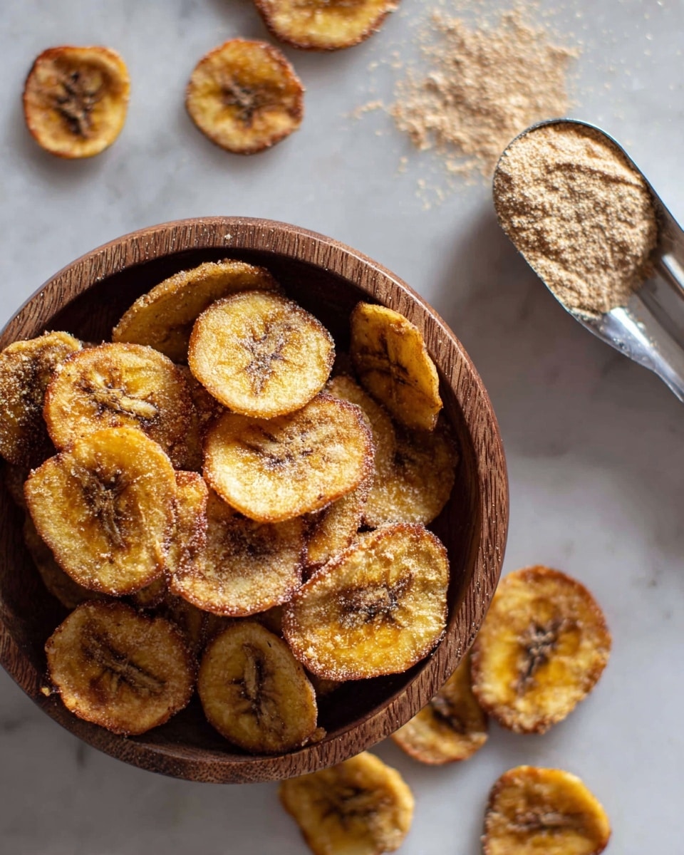A close-up of a wooden bowl filled with round, golden-brown banana chips that have a slightly crispy texture with darker spots in the center and edges, placed on a white marbled surface. Around the bowl, there are a few scattered banana chips, and a metal measuring spoon holding a light brown powder is positioned near the top right, with some of the powder sprinkled lightly on the marbled surface below. The overall lighting brings out the warm tones of the banana chips and the fine granules of the powder, giving a fresh and inviting look. photo taken with an iphone --ar 4:5 --v 7