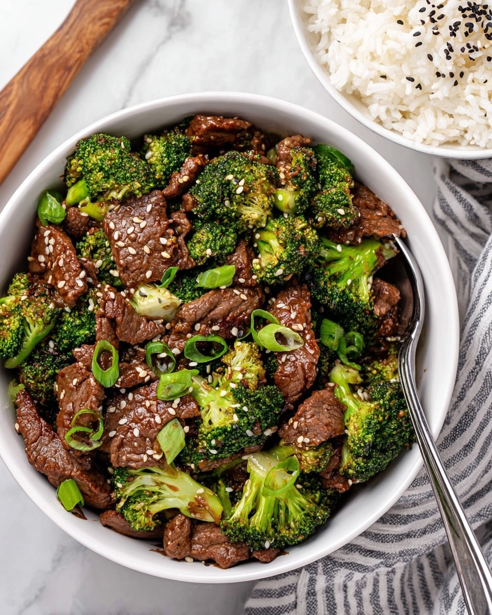 A white bowl filled with stir-fried beef and broccoli. The beef pieces are medium brown and tender-looking, mixed evenly with bright green broccoli florets. The dish is sprinkled with white and black sesame seeds and thin green onion rings. A metal spoon rests inside the bowl on the right side. Next to this bowl, at the top right, there is a white bowl of plain cooked white rice with some black sesame seeds on top. The whole scene is set on a white marbled surface with a striped cloth near the bottom right corner. photo taken with an iphone --ar 4:5 --v 7