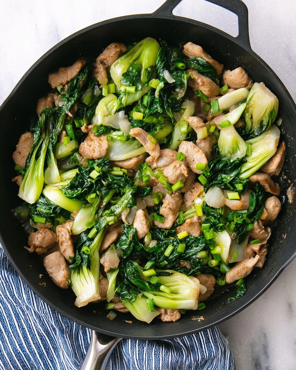 The image shows a black pan filled with a mix of light brown cooked meat pieces and bright green bok choy with leafy tops and crunchy stems. Light green chopped scallions are scattered over the dish, adding color and texture contrast. The food looks juicy and tender with the bok choy fresh and slightly wilted from cooking. The pan rests on a white marbled surface with a blue striped cloth partially visible next to the handle. photo taken with an iphone --ar 4:5 --v 7