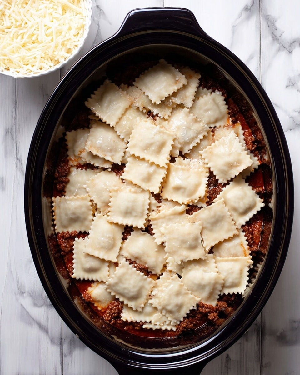 In a black oval cooking pot, there are three visible layers: the bottom layer is a reddish sauce spread evenly across the base, the middle layer is made of crumbled brown meat scattered on top of the sauce, and the top layer consists of square pasta pieces with light cream color and ruffled edges loosely covering the meat. The pot sits on a white marbled surface, and a white bowl filled with shredded cheese is partially visible near the bottom left corner of the image photo taken with an iphone --ar 4:5 --v 7