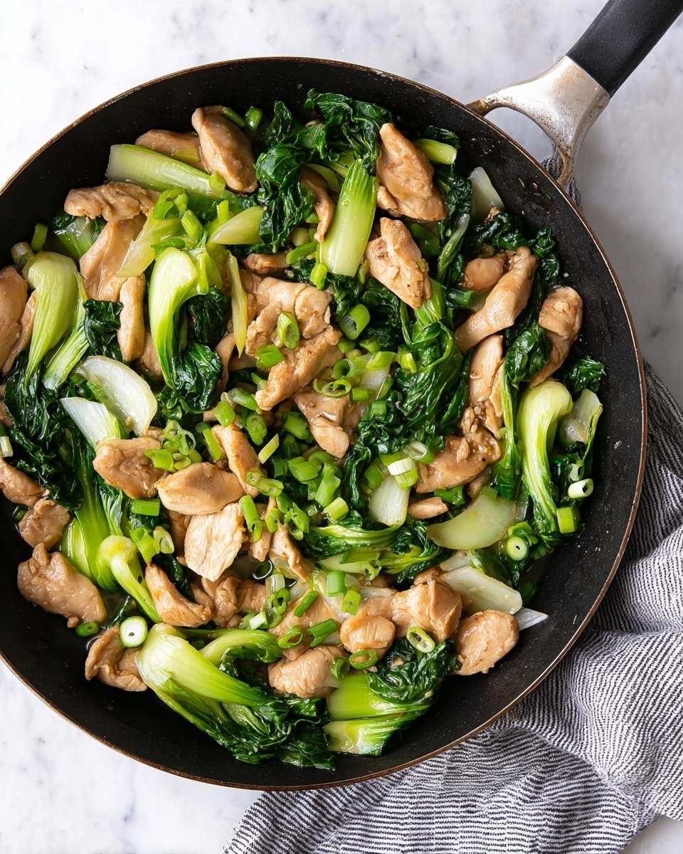 The image shows a black pan filled with stir-fried pieces of light brown chicken and bright green bok choy. The chicken slices are uneven in shape and lie across the pan mixed with fresh green bok choy leaves and stems. There are also small pieces of chopped green onions scattered on top, adding a fresh look. The pan is placed on a white marbled surface with a grey and white striped cloth nearby. The food has a lightly cooked texture with a mix of soft chicken and crisp green vegetables photo taken with an iphone --ar 4:5 --v 7