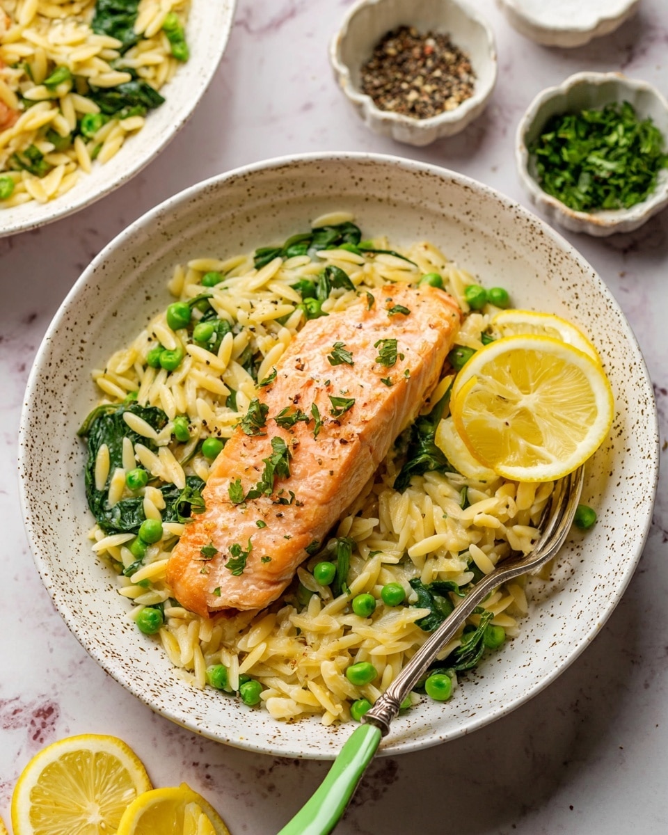 A white speckled shallow bowl filled with a bed of yellowish orzo pasta mixed with bright green peas and bits of cooked onion and spinach leaves, topped with a single piece of light orange cooked salmon sprinkled with small green herb pieces. Two thin lemon slices with green herb bits lie on the side of the salmon. A silver fork with a green handle partially rests in the pasta. The bowl sits on a white marbled surface, with small dishes of black pepper, salt, and chopped herbs visible in the background. photo taken with an iphone --ar 4:5 --v 7