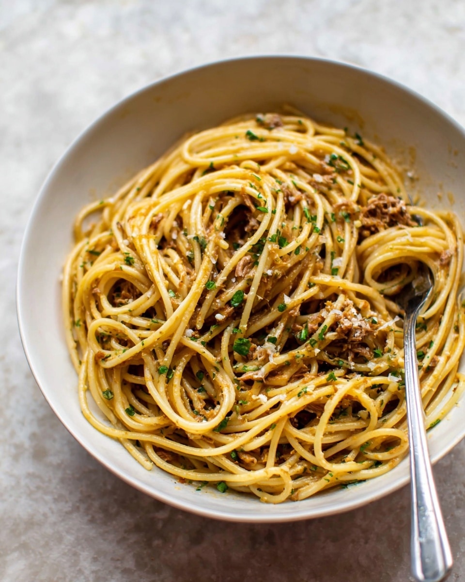 A round white bowl sits on a white marbled surface, filled with a single large layer of thick spaghetti noodles coated in light brown sauce with small bits of shredded meat and finely chopped green herbs scattered throughout. A silver fork rests inside the bowl on the right side, with its tines slightly buried under the noodles. The noodles show smooth and slightly shiny textures, with some strands loosely swirling and overlapping. The background is softly blurred, focusing attention on the bowl of pasta. photo taken with an iphone --ar 4:5 --v 7