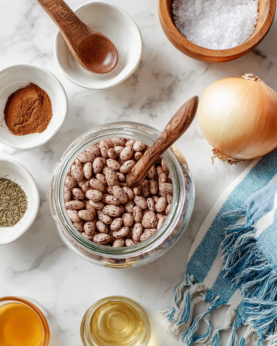 A clear glass jar filled with light brown beans with darker brown spots sits in the middle, with a wooden spoon resting inside the jar. Surrounding the jar are small white bowls, one with brown powder, another with green dried herbs, and a light wooden bowl with coarse white salt. A large white onion is positioned to the right, near a blue and white striped cloth with fringes. A small glass container with light golden liquid is placed near the bottom center. All items rest on a white marbled surface. photo taken with an iphone --ar 4:5 --v 7