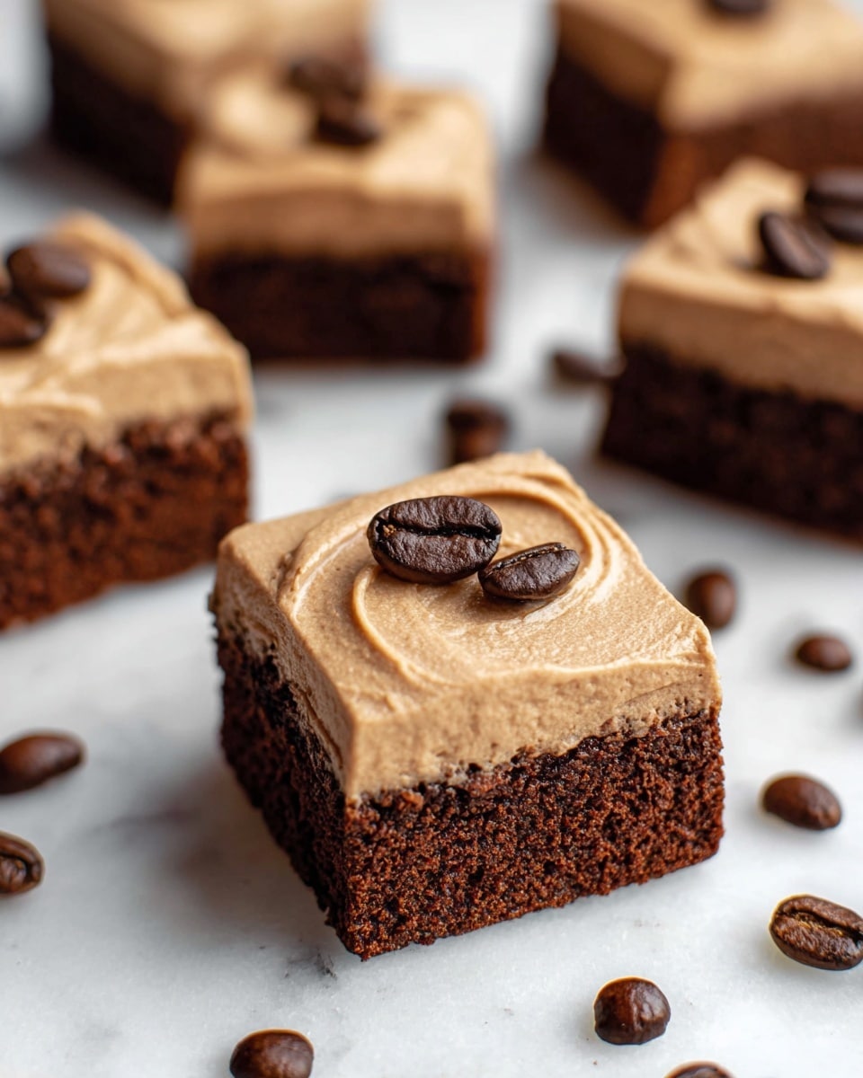 The image shows square pieces of chocolate brownies, each topped with a thick layer of smooth, light brown frosting. The frosting has a soft, creamy texture with light ridges and three dark brown coffee beans carefully placed on top of the nearest brownie piece in the center. The brownies have a rich, dark brown, slightly crumbly base layer. Coffee beans are scattered on the white marbled surface around the brownies, adding visual contrast and texture. The focus is on one brownie piece in the foreground, with several others slightly out of focus in the background. photo taken with an iphone --ar 4:5 --v 7