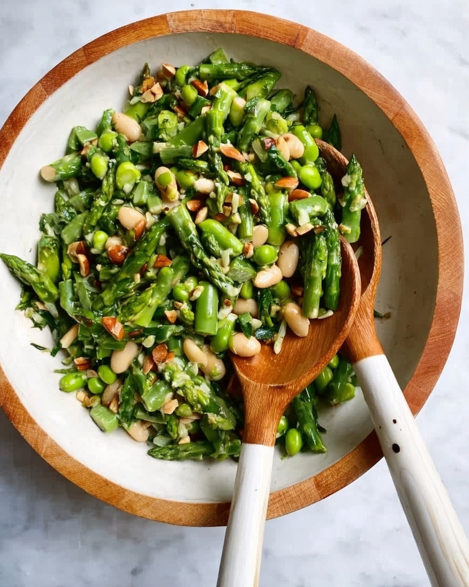 A white bowl with a thin wooden rim holds a vibrant salad made of chopped green asparagus, white beans, and scattered pieces of nuts. Two wooden spoons with white handles rest inside the bowl, partially covered by the salad. The grains and vegetables show a mix of smooth and rough textures. The bowl is on a white marbled surface. photo taken with an iphone --ar 4:5 --v 7