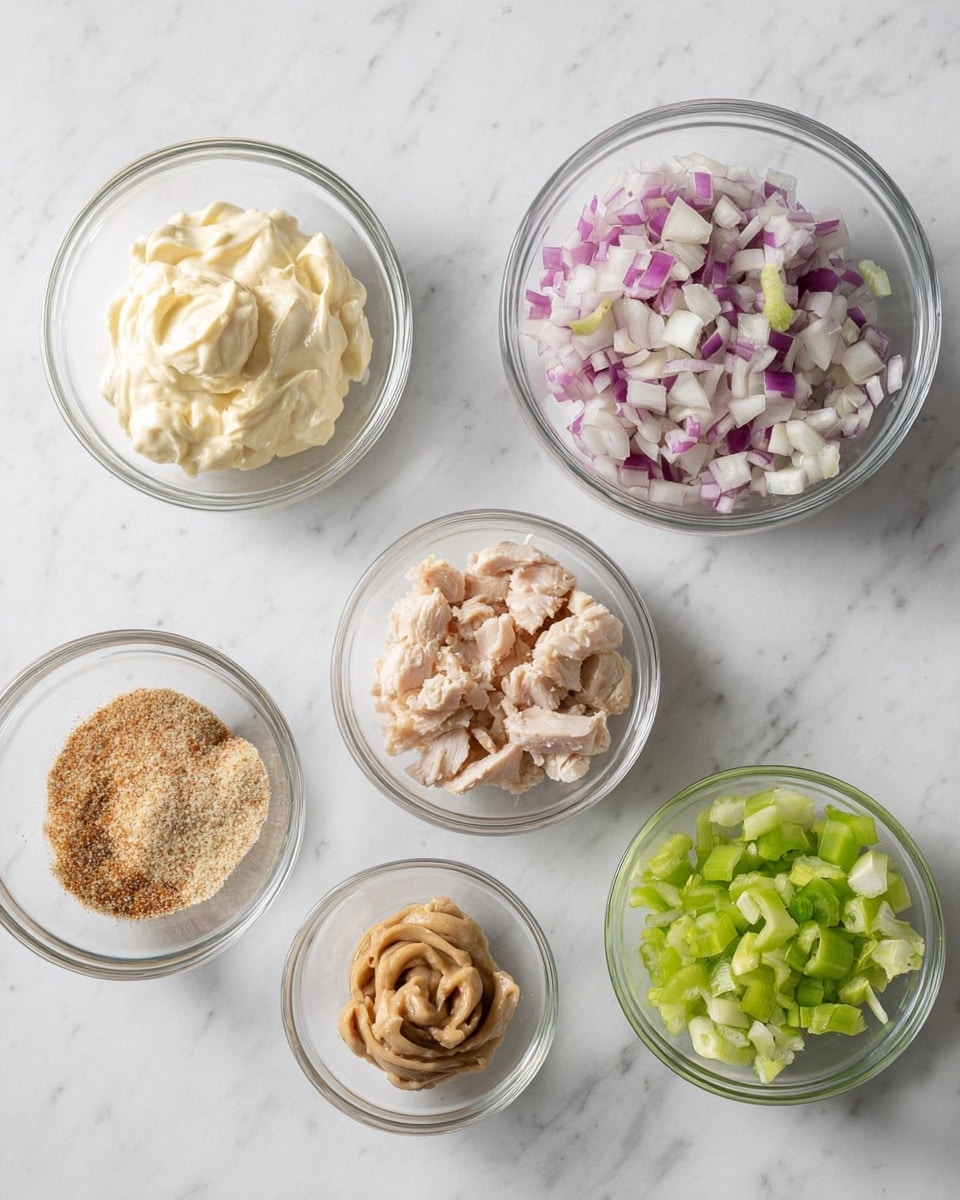 The image shows six clear glass bowls placed on a white marbled surface. The top row has three bowls: the left one filled with creamy mayonnaise that has a smooth and thick texture, the middle one containing finely chopped red onions with purple and white pieces, and the right bowl loaded with small pieces of cooked chicken that are light brown and white. The bottom row has three smaller bowls: the left one holding a light brown spice mix with a sandy texture, the middle bowl filled with a light brown grainy mustard paste shaped in a twist, and the right one contains finely chopped green celery pieces. The bowls are arranged neatly with even spacing. Photo taken with an iphone --ar 4:5 --v 7