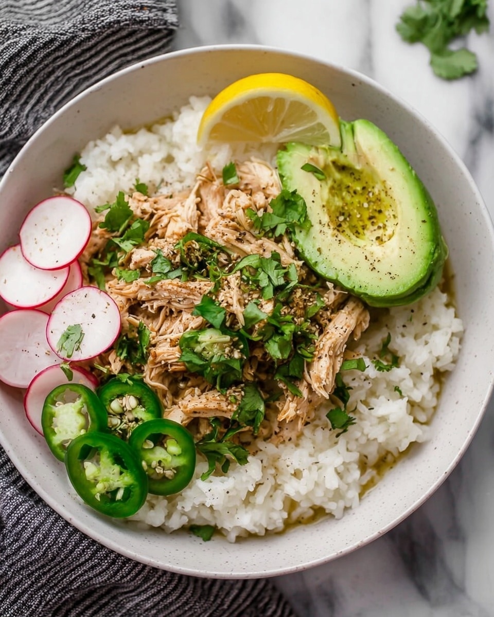 The dish is served in a white bowl on a white marbled surface with a striped cloth nearby. It has three main layers: a base layer of white rice with a soft texture, topped with shredded light brown cooked chicken in the middle. Over the chicken, there are sliced green jalapeños and radishes on the left side, fresh green cilantro sprinkled all over, and on the right, three slices of light green avocado sprinkled with black pepper. A lemon wedge sits on top center, adding a yellow accent to the dish. photo taken with an iphone --ar 4:5 --v 7