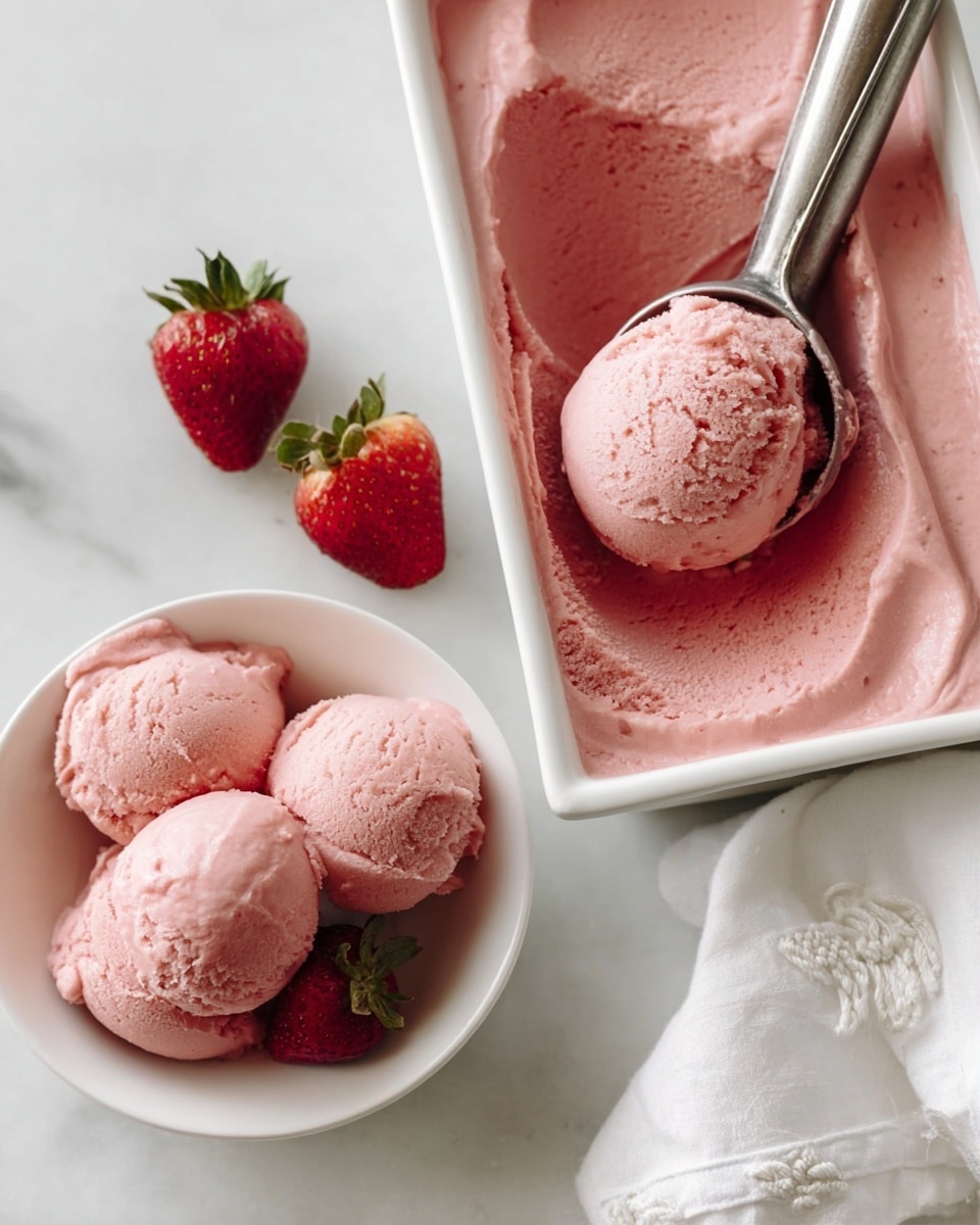 A white rectangular container filled with smooth pink strawberry ice cream, with one rounded scoop partially lifted by a metal ice cream scooper. Below, a white bowl holds four rounded scoops of the same pink ice cream with a soft and creamy texture, with a silver spoon resting inside. Two fresh red strawberries with green leafy tops are placed on the white marbled surface near the bowl. A white cloth napkin with delicate embroidery is also on the right side of the frame. photo taken with an iphone --ar 4:5 --v 7