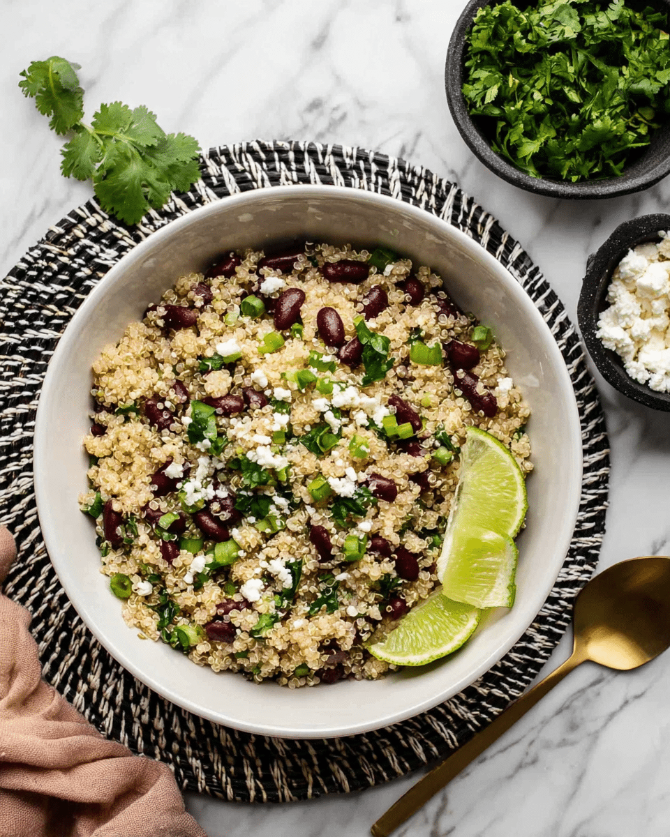 A white bowl filled with a quinoa salad showing three main layers: the base layer is light beige cooked quinoa with its grainy texture; the middle layer is scattered dark red kidney beans adding bursts of color; the top layer includes chopped green onions and fresh cilantro leaves giving bright green highlights, plus small white crumbles of cheese mixed throughout. The bowl is garnished with two lime wedges on the side. The bowl rests on a woven black and white placemat over a white marbled surface. Nearby there is a white bowl filled with fresh cilantro and a small black bowl with white cheese crumbles. A gold spoon is placed on the right side, and a woman’s hand is holding the woven placemat on the left. Photo taken with an iphone --ar 4:5 --v 7