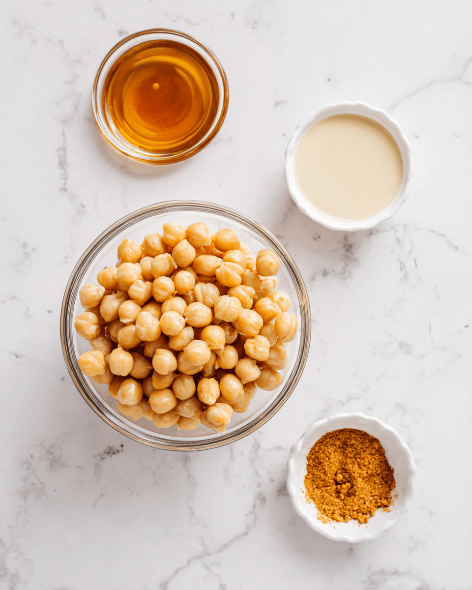 A clear glass bowl filled with light beige chickpeas sits in the center on a white marbled surface. Around it, there are three small white bowls: one on the left holding a glossy amber liquid, one at the top right with a pale creamy liquid, and one at the bottom right containing a fine orange-brown spice powder. The arrangement is neat and simple, focusing on the ingredients with soft natural light. Photo taken with an iphone --ar 4:5 --v 7